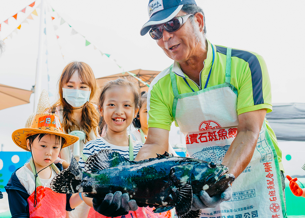遊客來到蘇班長安心漁場體驗「一日漁夫」活動，蘇班長帶小朋友一起抱石斑魚。(圖片提供/新港社合)
